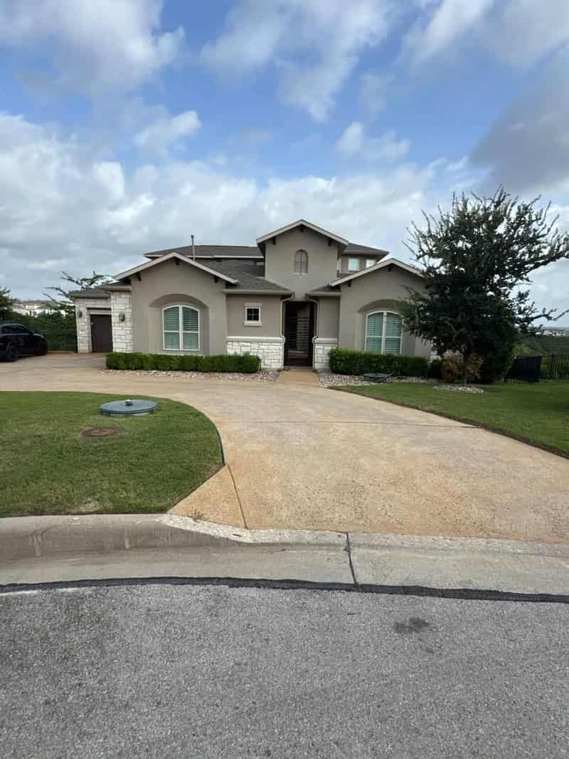Large two-storey stone and stucco house in Lakeway with a circular driveway, photographed under a gathering sky before the roof survey
