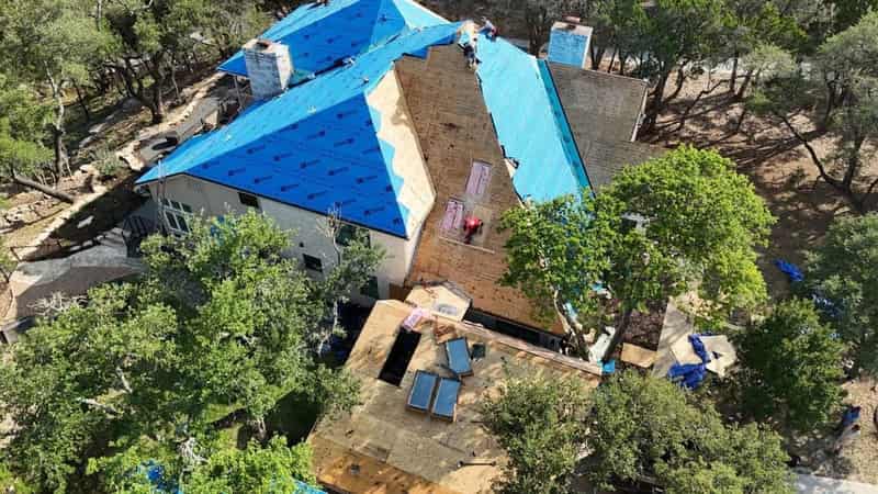 Aerial view of a large Wimberley property mid re-roof, with tear-off, bare decking and blue synthetic underlayment all visible