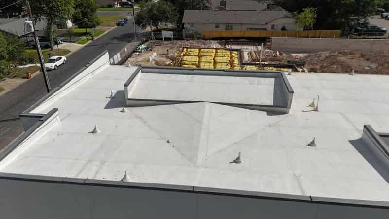 Aerial view of a white TPO commercial flat roof with pipe boots, beside an active build site