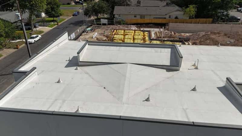 Aerial view of a white TPO commercial flat roof with pipe boots beside an active build site
