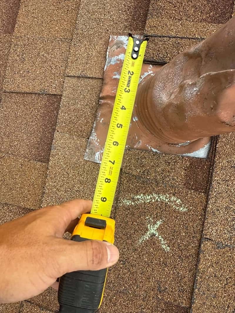 Tape measure checking clearance around a rubber pipe boot with a chalk X mark nearby