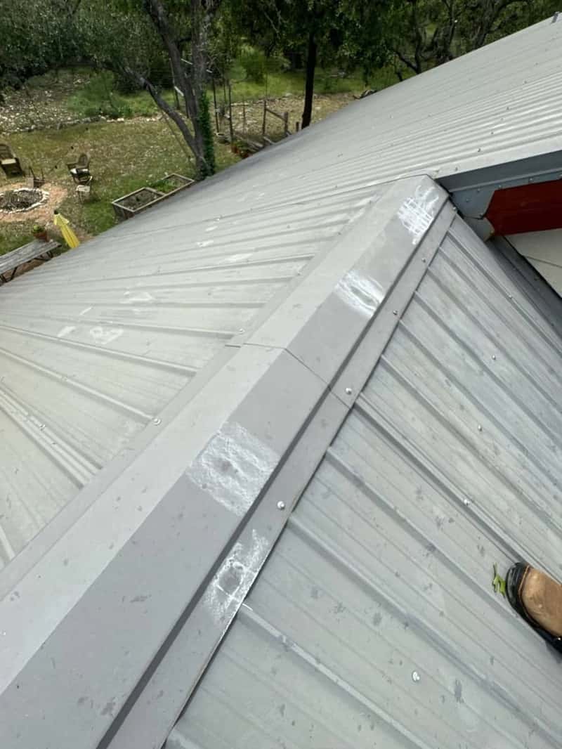 Standing view on a metal roof ridge with chalk-marked hail hits and a backyard fire pit below
