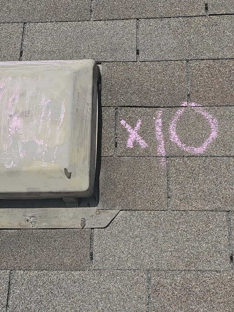 Roof vent boot next to pink chalk marks reading X O on shingles