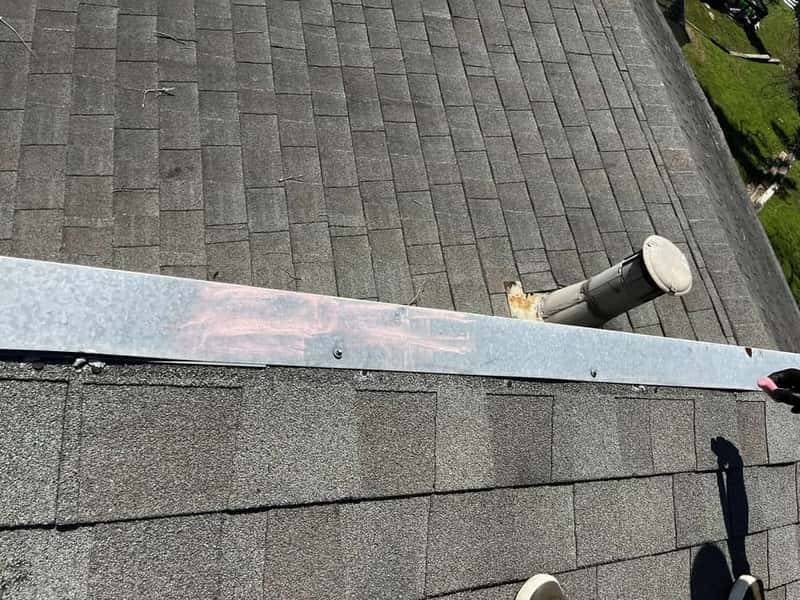 Shingle roof with a rust-streaked plumbing vent stack overlooking a wooded yard