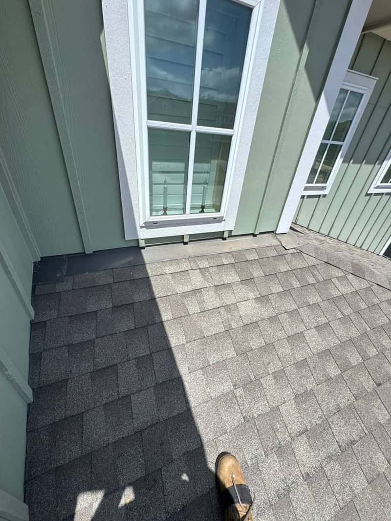 Roof-to-wall shingle transition beneath a second-story window on a green siding house