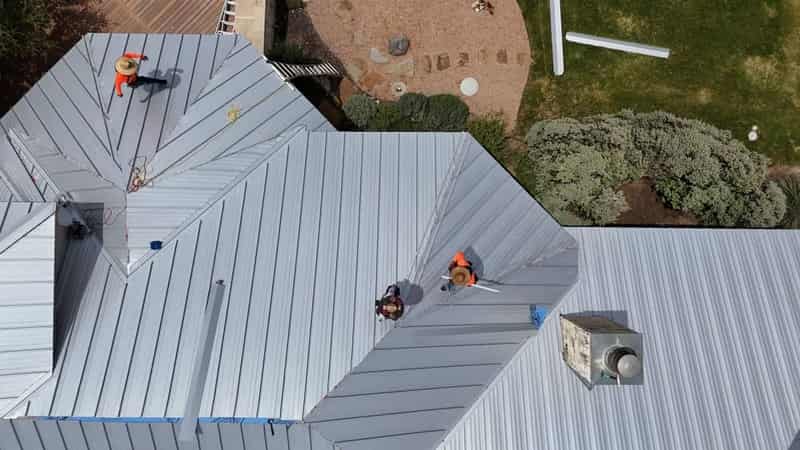 Wide view of a standing-seam metal roof going on in Leander, panel seams running to the ridge