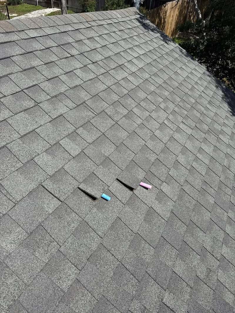 Roof shingles with blue and pink marker tabs flagging spots for repair