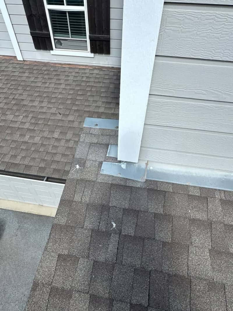Roof-to-wall step flashing metal installed against gray siding corner