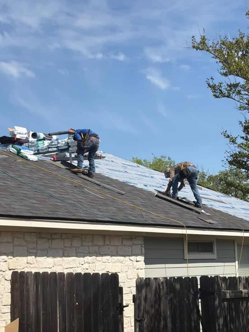 Two Waypoint roofers installing shingles side by side on a steep roof, backs to the camera