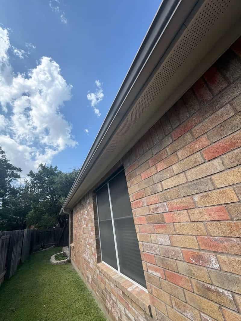 Perforated soffit vents and gutter running along a brick home's eave above a window