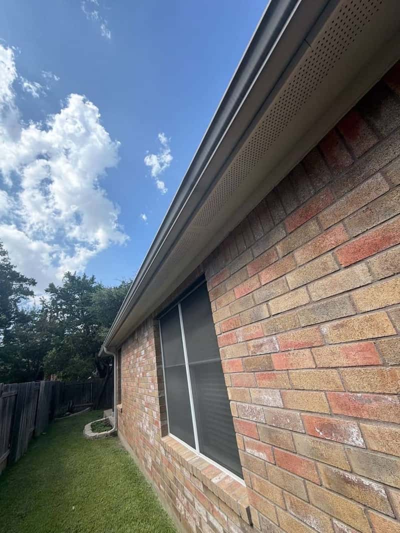 Perforated soffit vents and gutter along a brick home's eave above a window