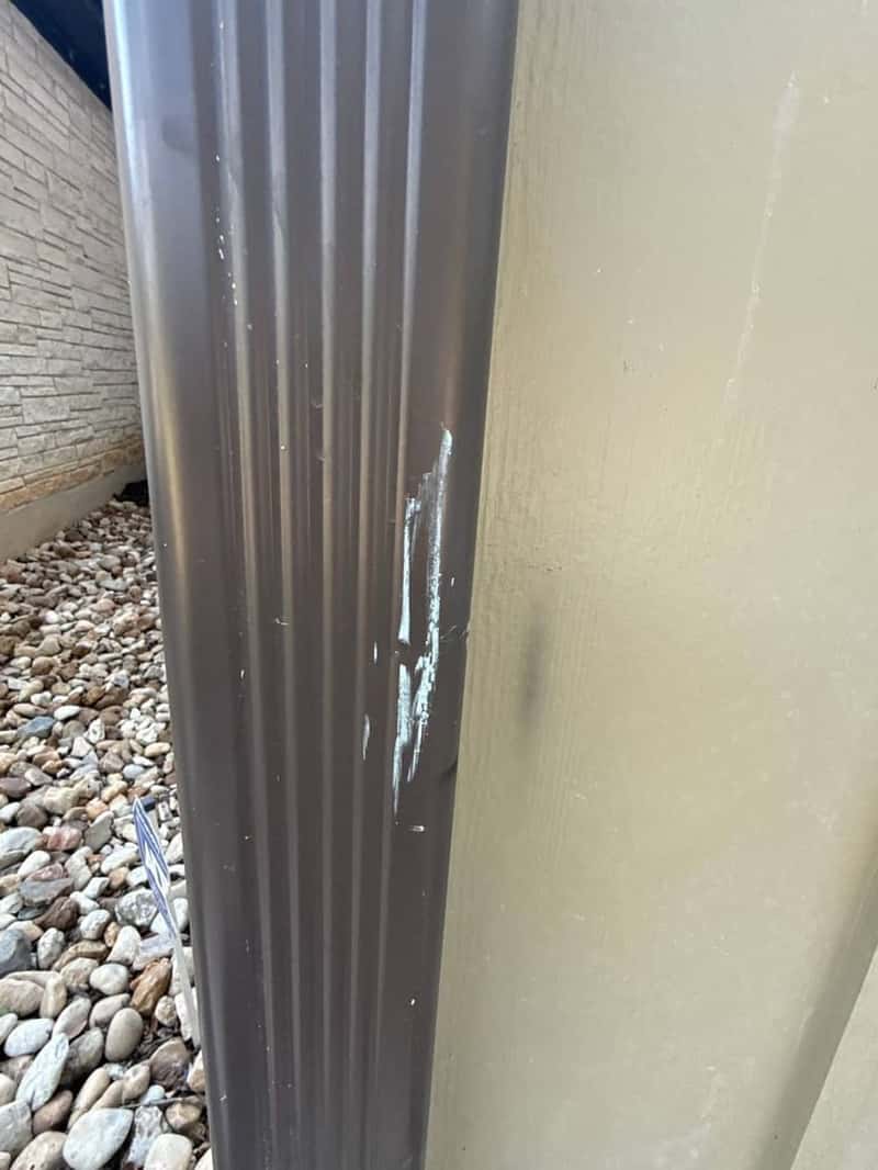 Brown downspout corner closeup against tan stucco siding