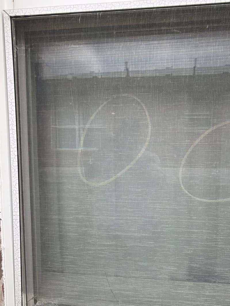 Window screen mesh with chalk circles marking hail impact points