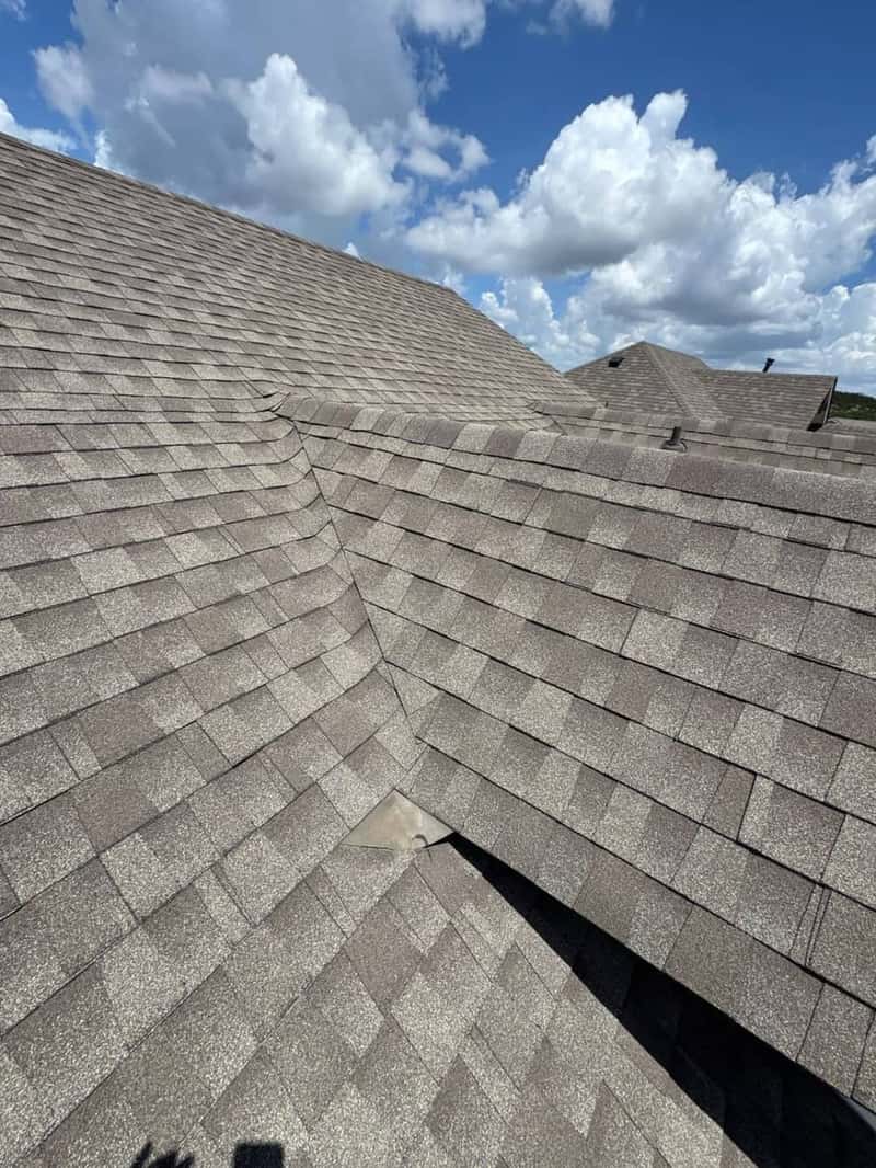 Wide aerial view of a gray shingle hip roof against a bright blue sky with clouds
