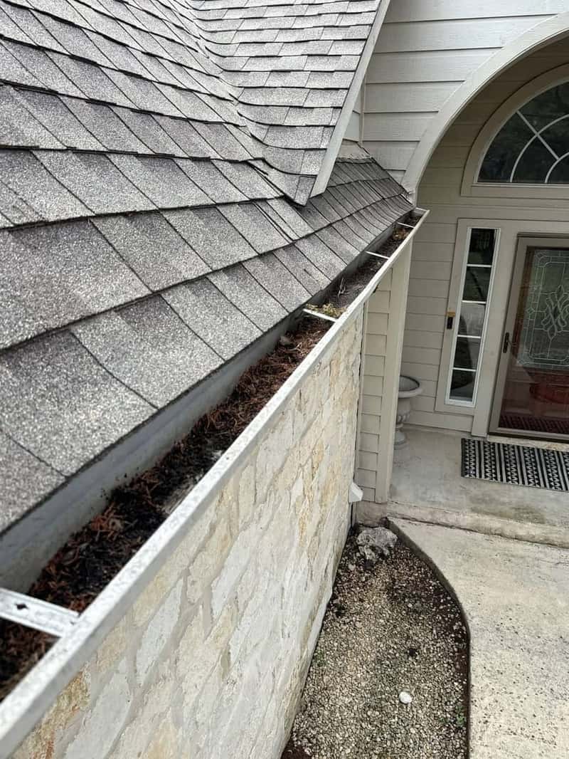 Clean gutter and shingle roofline above an arched stone entryway